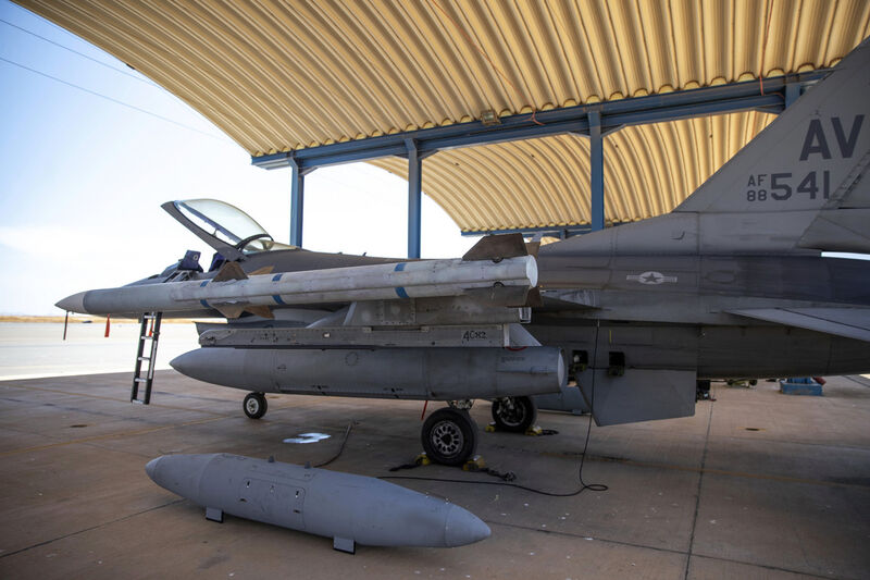 An F-16 in a shelter with a travel pod on the ground beside it, ready to load