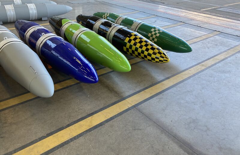 Freshly painted travel pods lined up on a hangar floor, in blue, green, and black and yellow checks