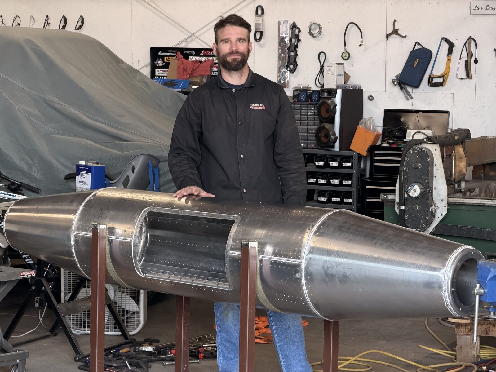 Mark standing beside pod number 001, his first completed travel pod, in the shop