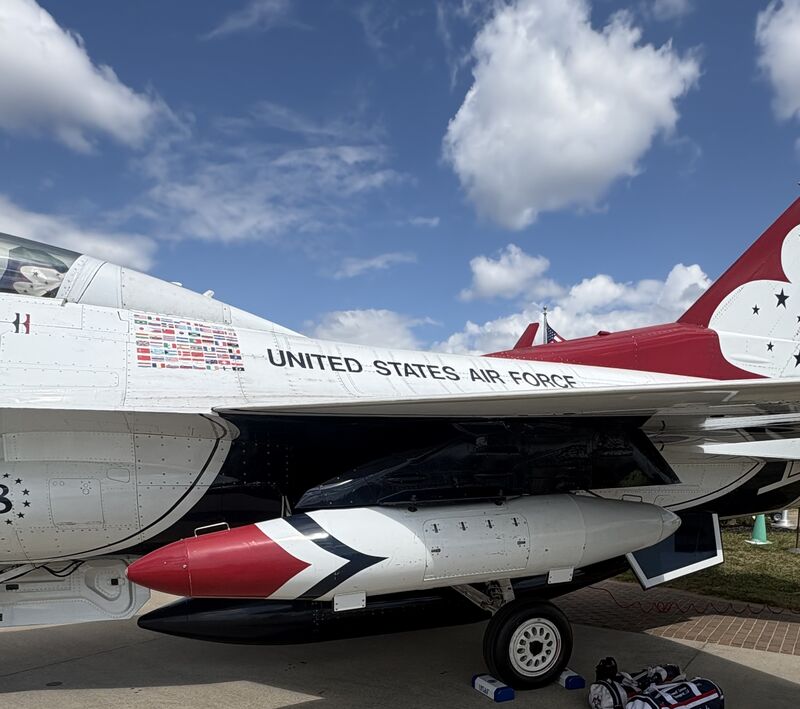 A Thunderbirds F-16 with a travel pod painted red, white and blue under its wing