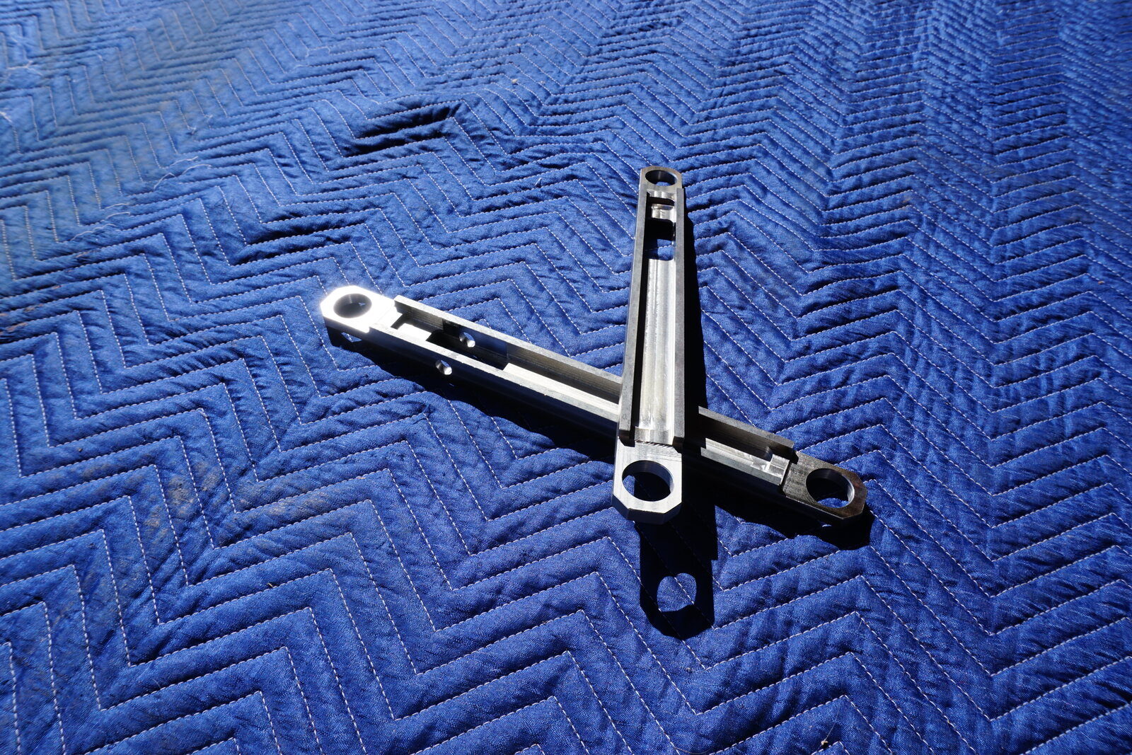 Two machined control arms on a blue moving blanket